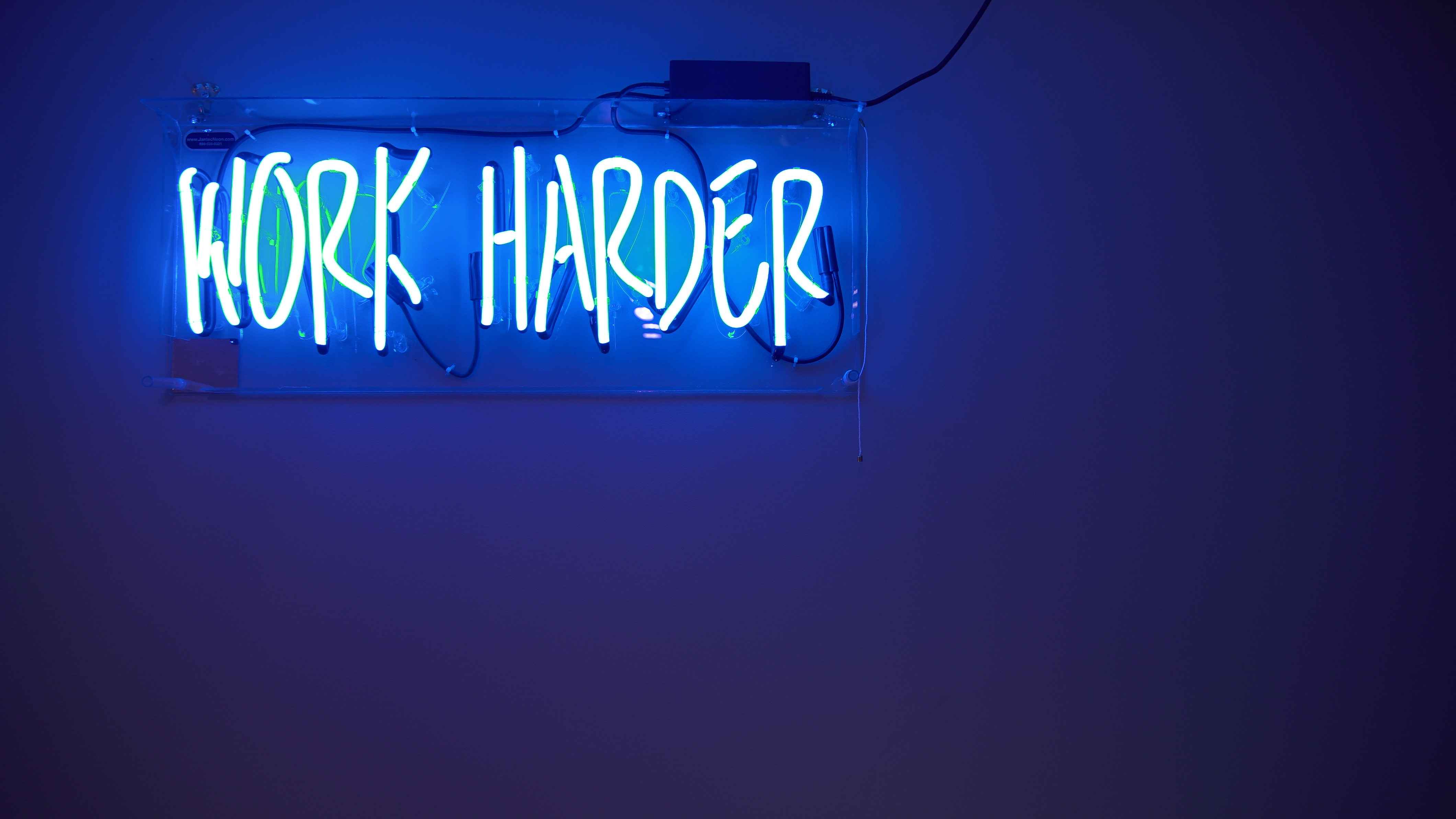 A neon sign saying "Work harder"